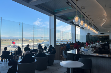 a group of people sitting at tables in a room with glass walls and a large window