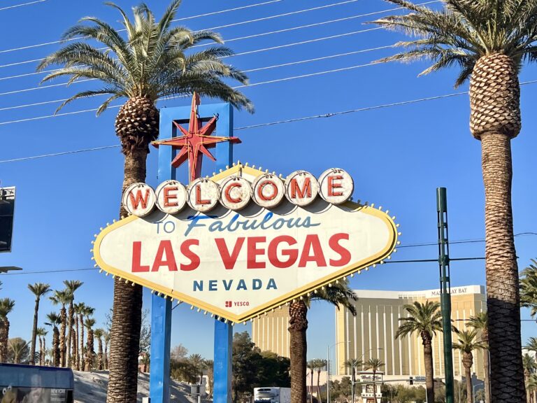 a sign with palm trees and buildings in the background with Welcome to Fabulous Las Vegas sign in the background