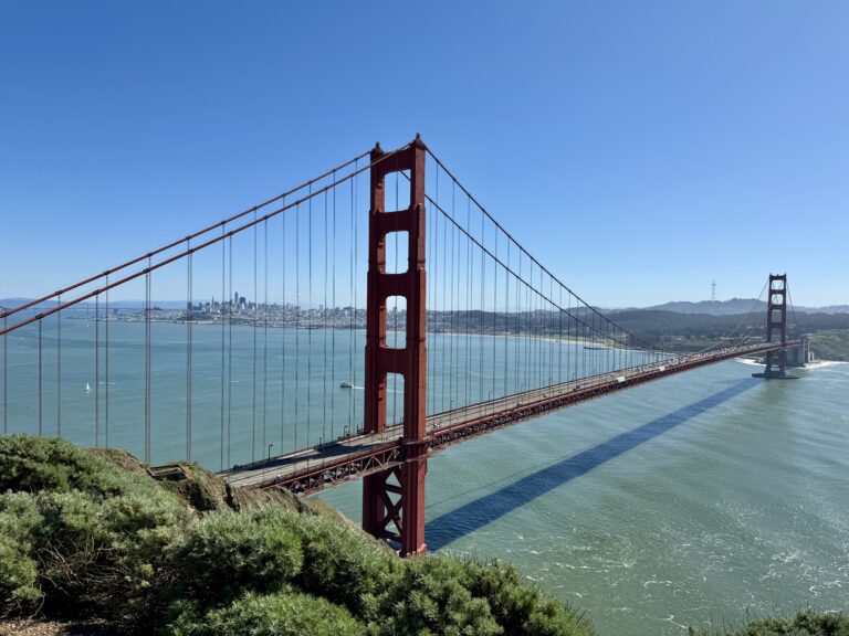 Golden Gate Bridge over water with trees and a city in the background