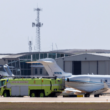 a green truck and plane on a runway